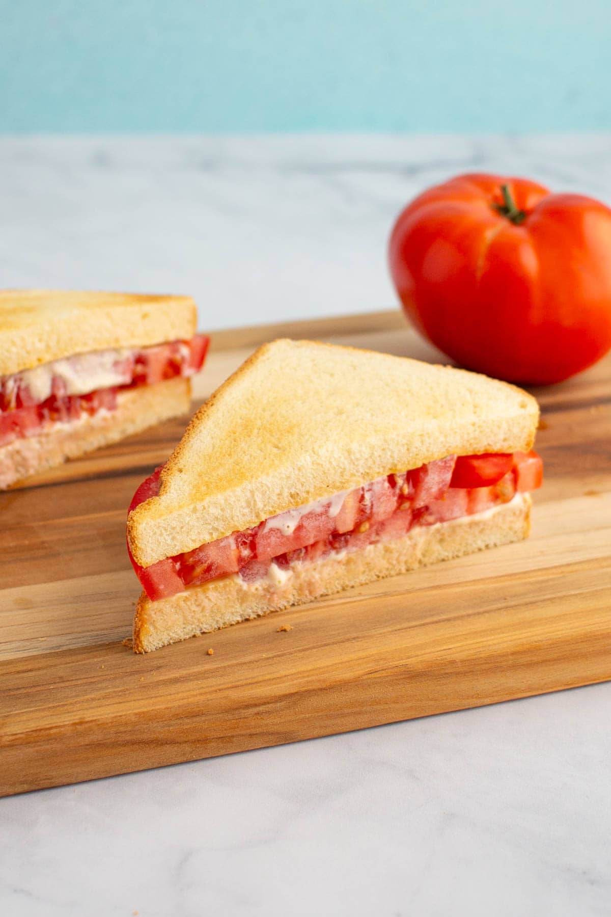 An ultimate umami tomato sandwich cut in half on a cutting board, with a tomato nearby.