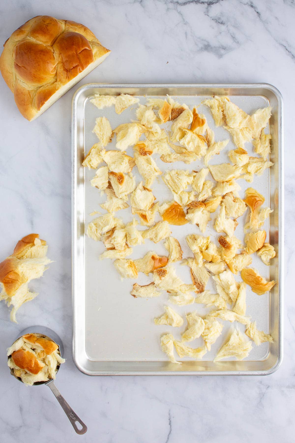 A loaf of challah torn into pieces on a baking sheet.