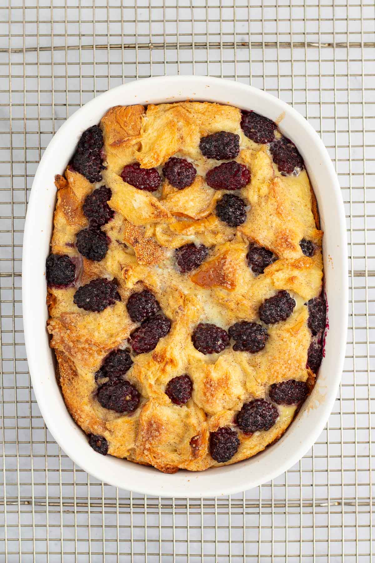 A dish of baked Blackberry Bread Pudding on a cooling rack.