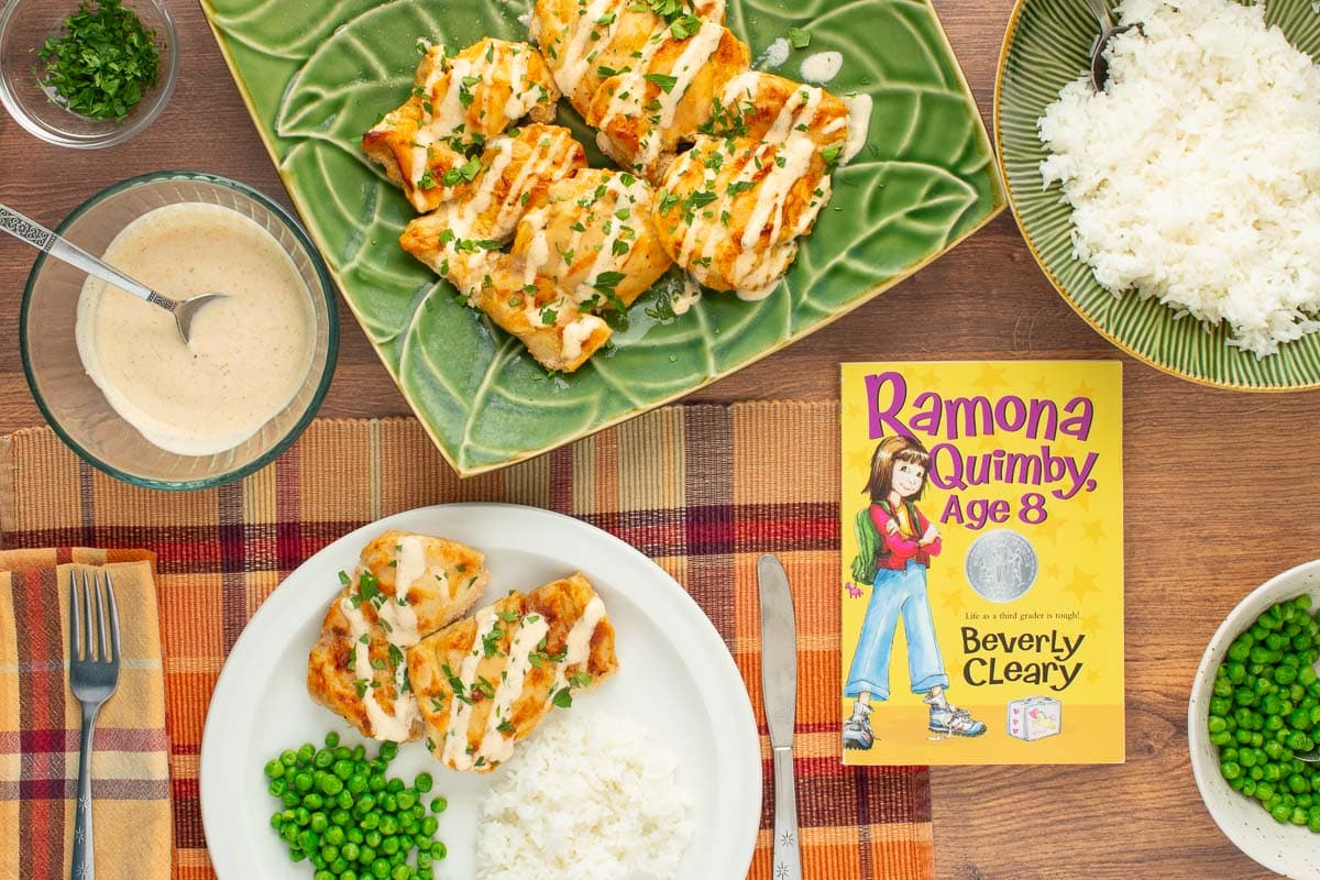 The cover of the book "Ramona Quimby, Age 8" next to a plate and a platter of Juicy Yogurt-Baked Chicken, along with bowls pf yogurt sauce, rice, and peas.