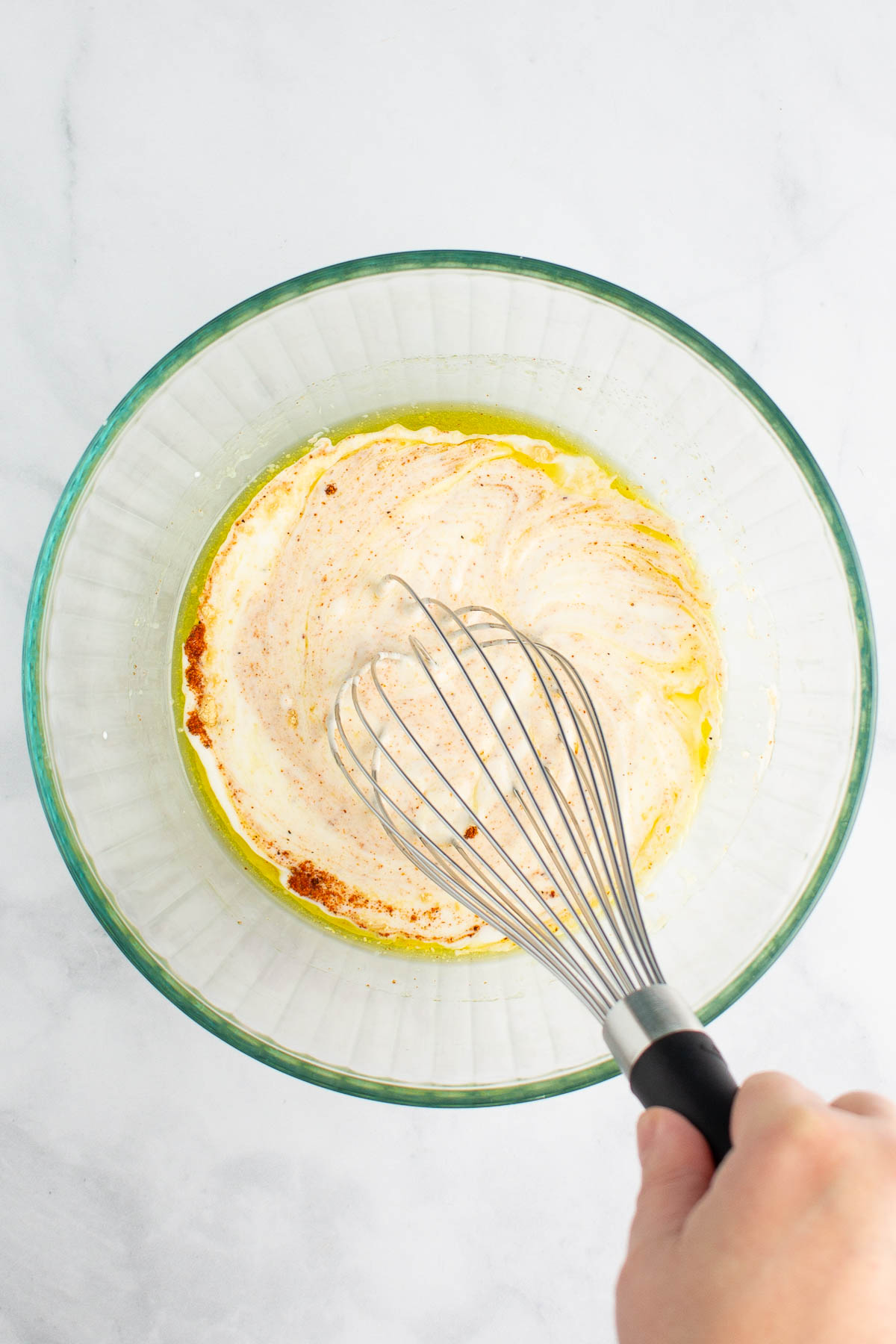 A hand whisking together yogurt sauce in a bowl.