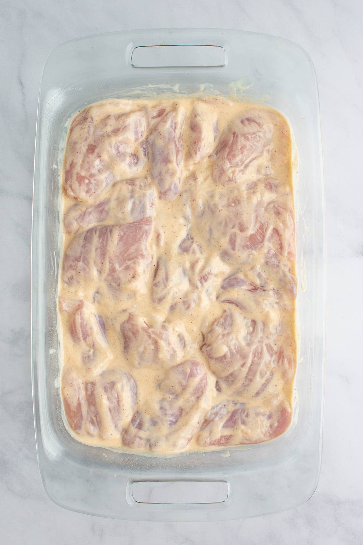 Chicken thighs coated in yogurt sauce in a baking dish.