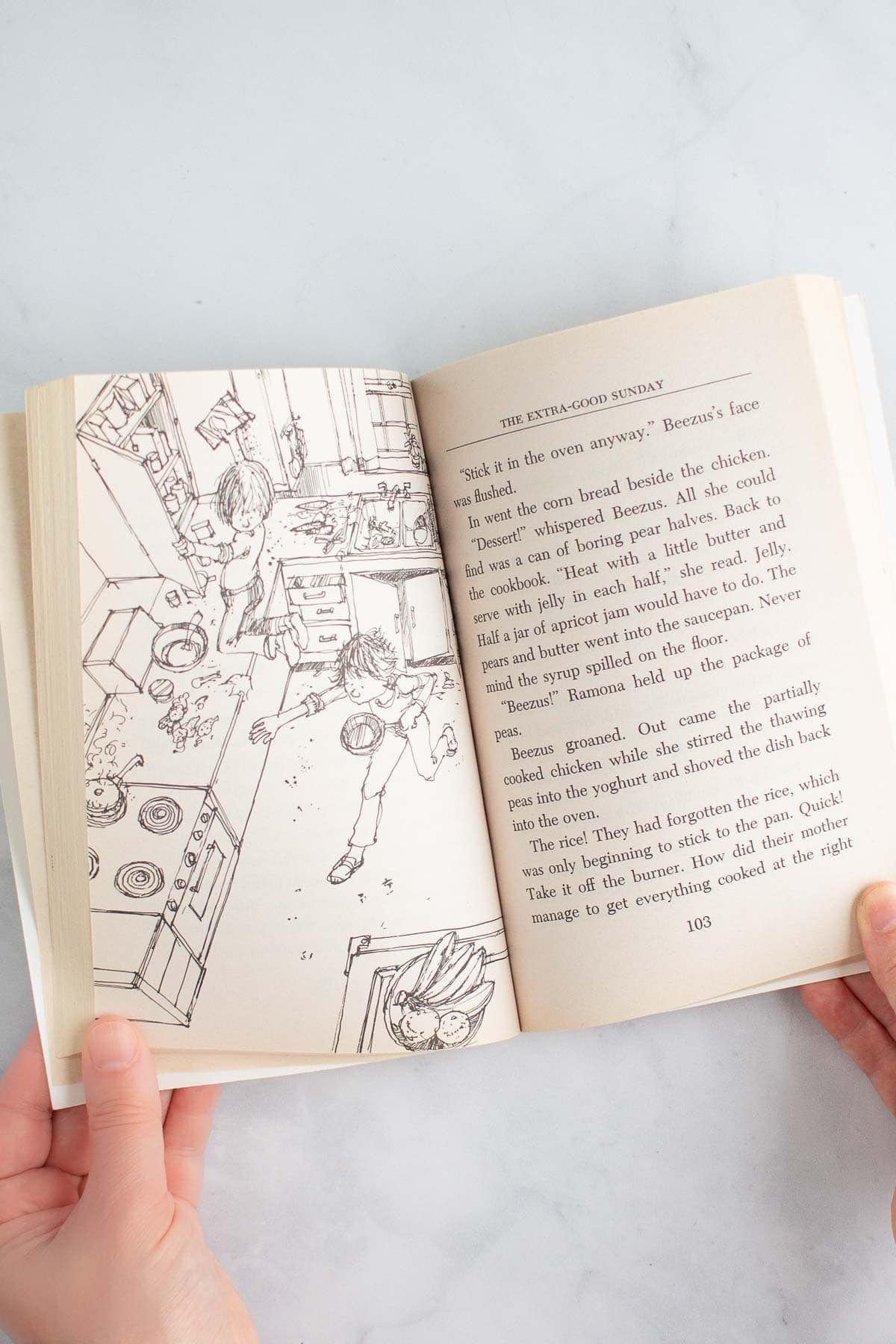 Two hands holding open the book "Ramona Quimby, Age 8" to a page with an illustration.