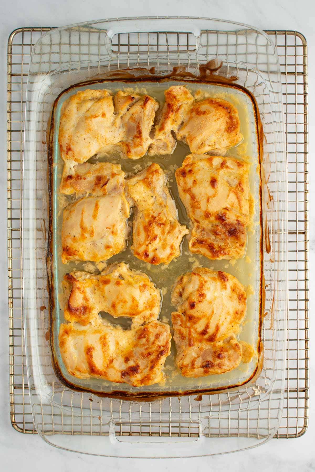 Baked chicken thighs in a baking dish on a cooling rack.