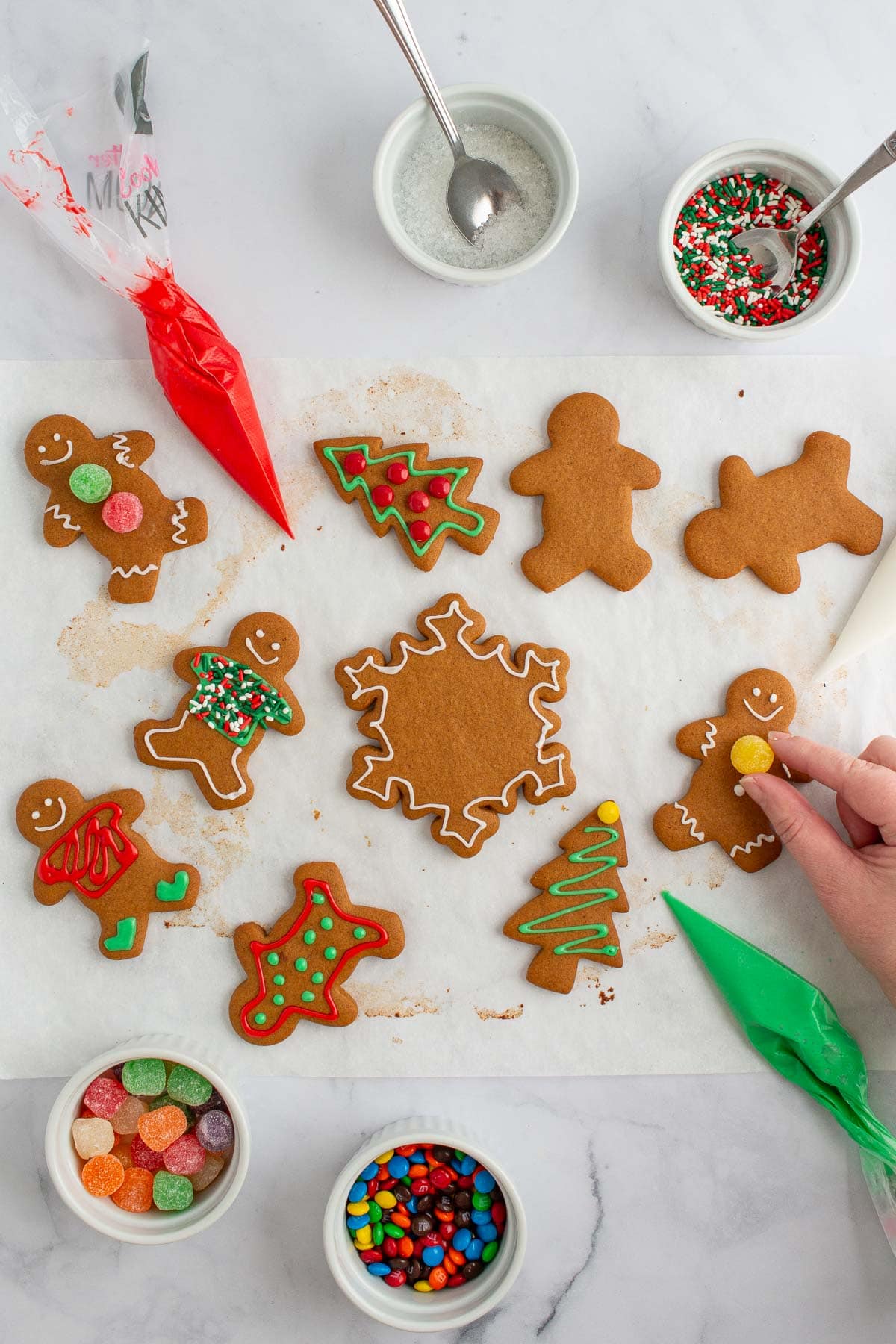 A hand adding decorations to baked easy gingerbread cookies.