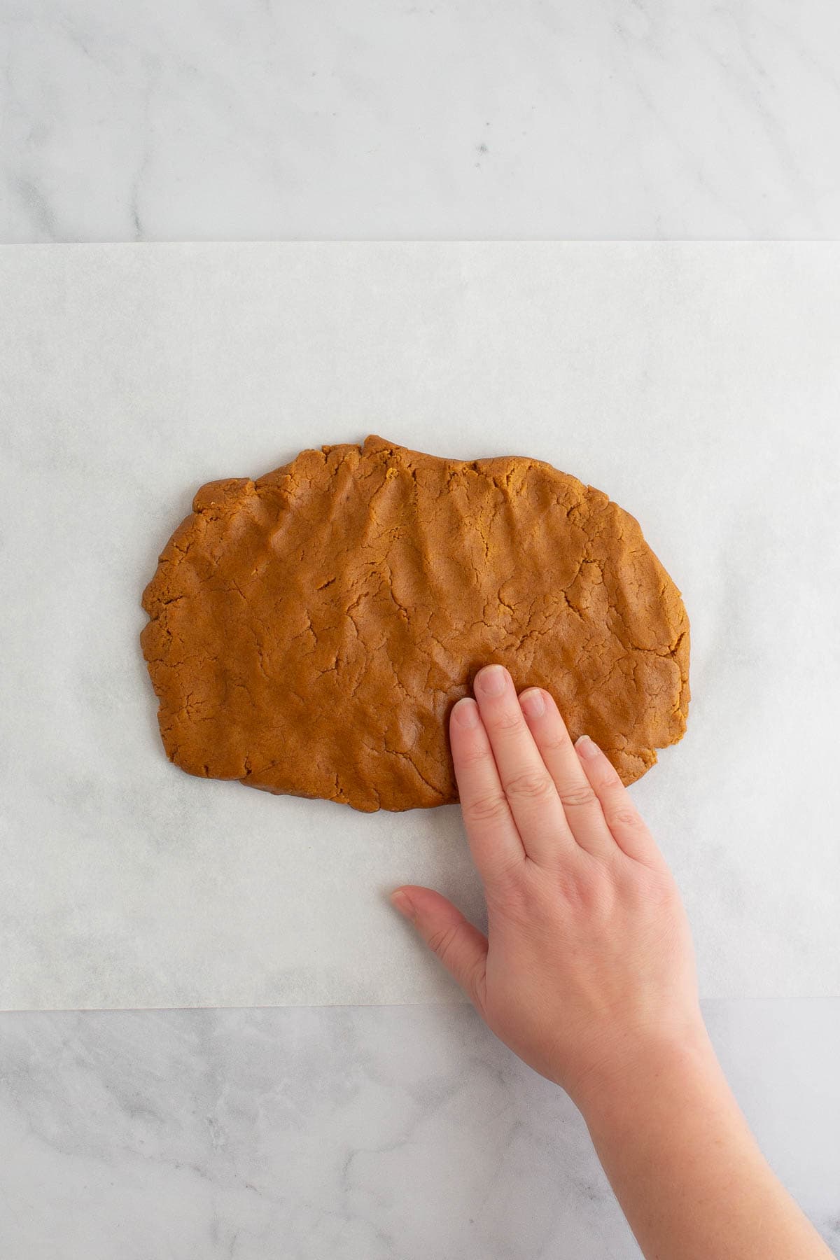 A hand patting out dough for easy gingerbread cookies on a sheet of parchment paper.