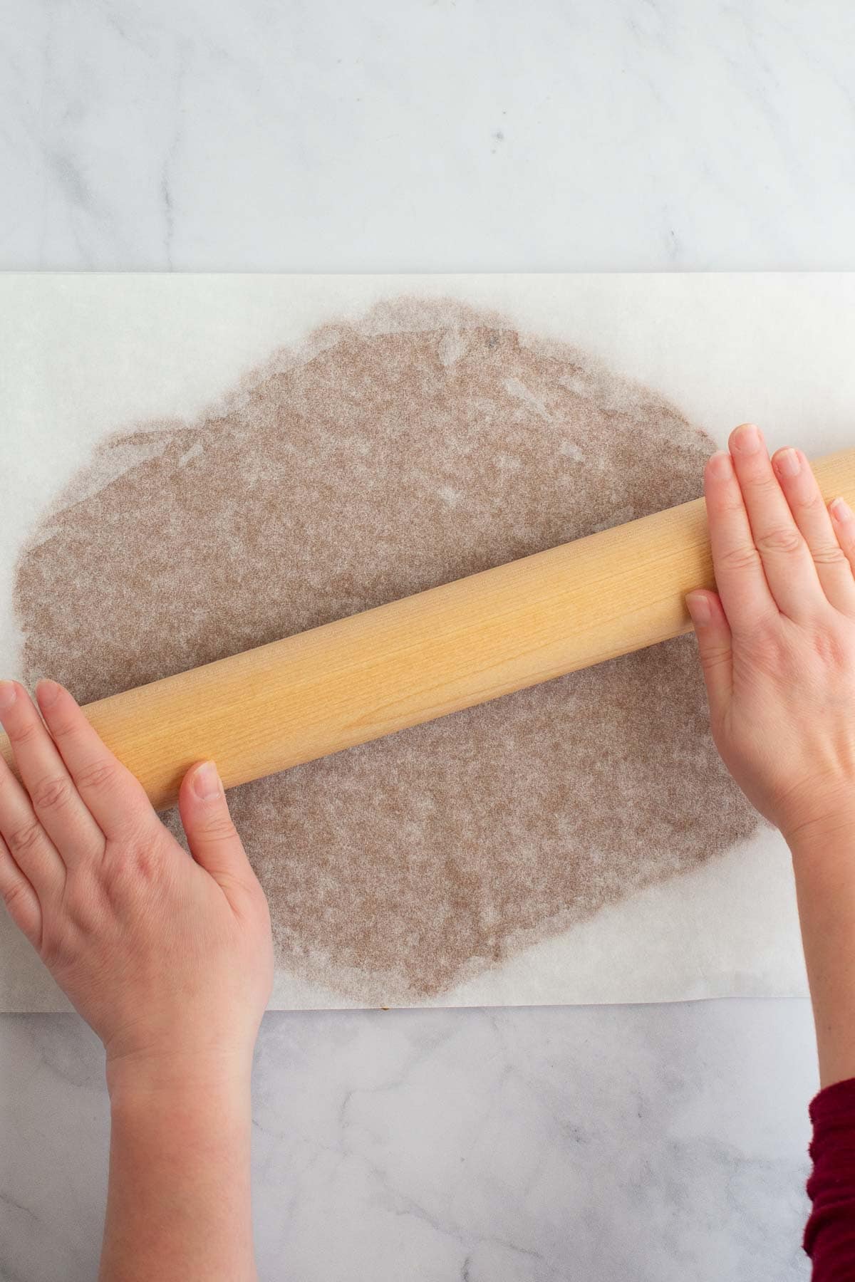 Hands using a rolling pin to roll out dough for easy gingerbread cookies.