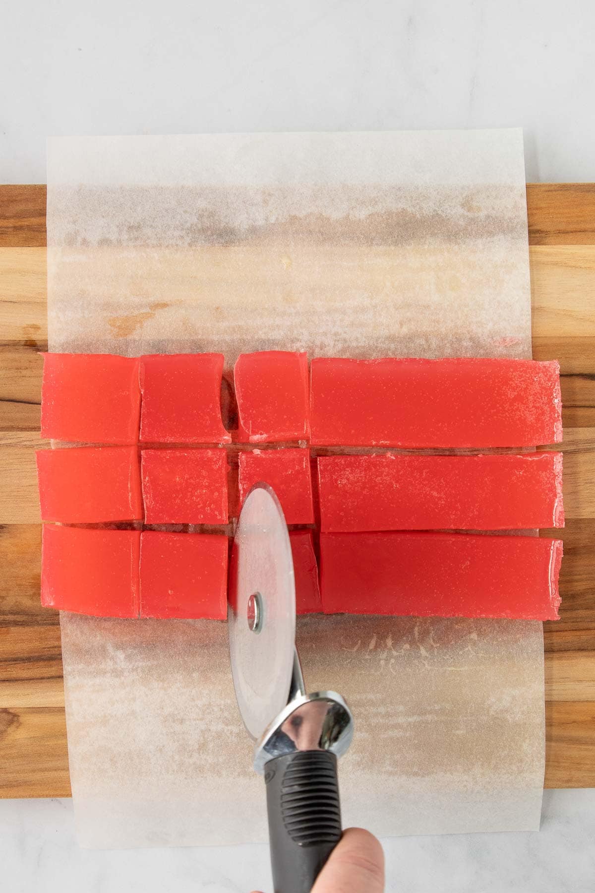 A hand using a pizza cutter to cut Turkish Delight into pieces.