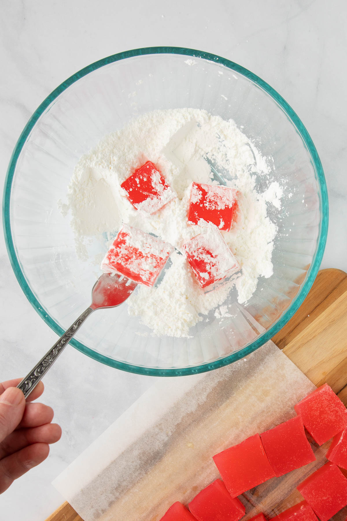 A hand using a fork to toss Turkish Delight in a powdered sugar mixture in a bowl.