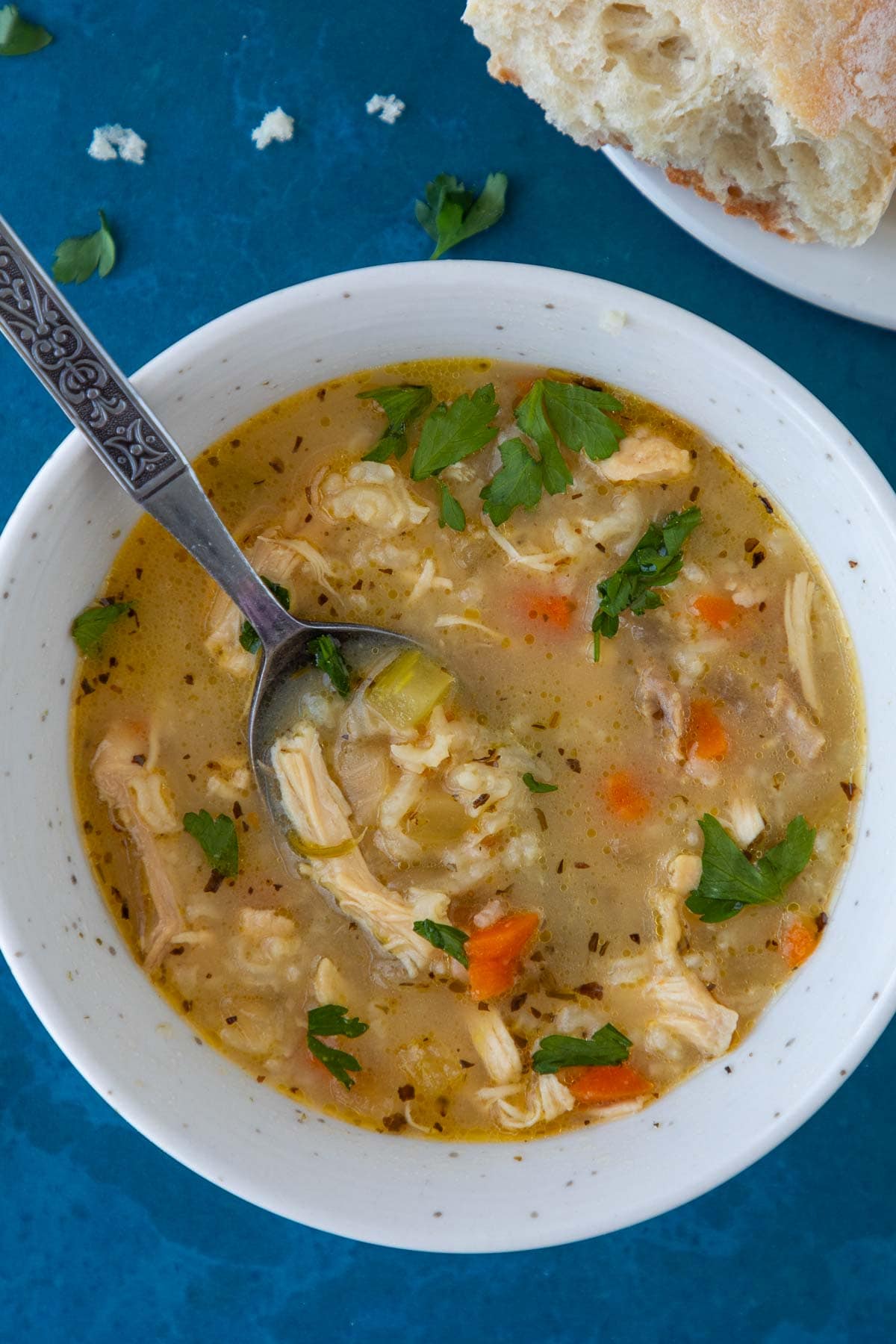 A bowl of chicken soup with rice, with a piece of bread on the side.