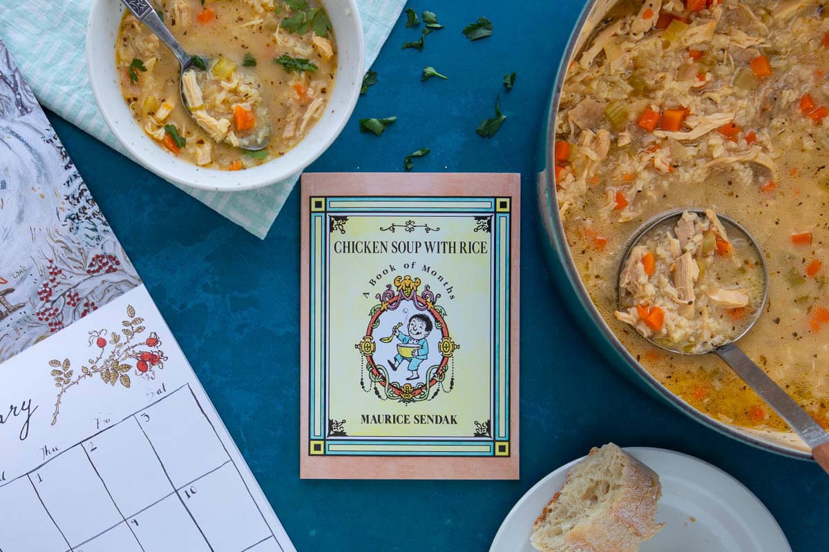 The cover of the book Chicken Soup with Rice next to a bowl and pot of chicken soup, with a calendar and bread on the side.