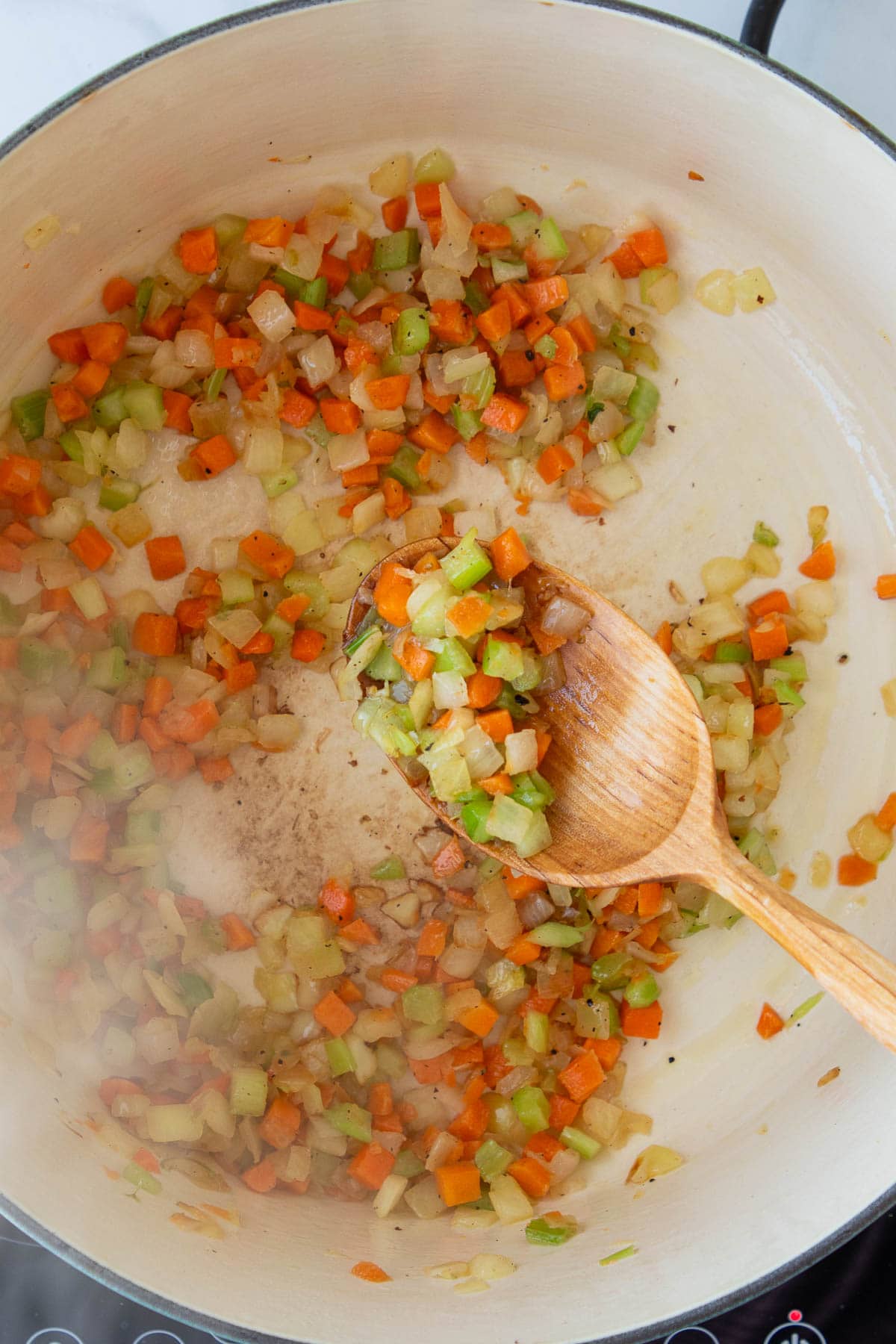 A wooden spoon stirring mirepoix in a pot.