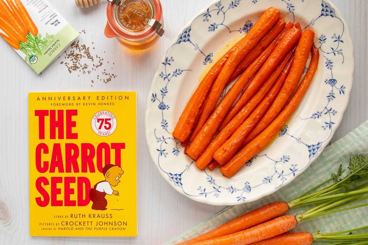 The cover of the book The Carrot Seed next to a platter of honey roasted carrots, a packet of carrot seeds, a bunch of fresh carrots, and a jar of honey.