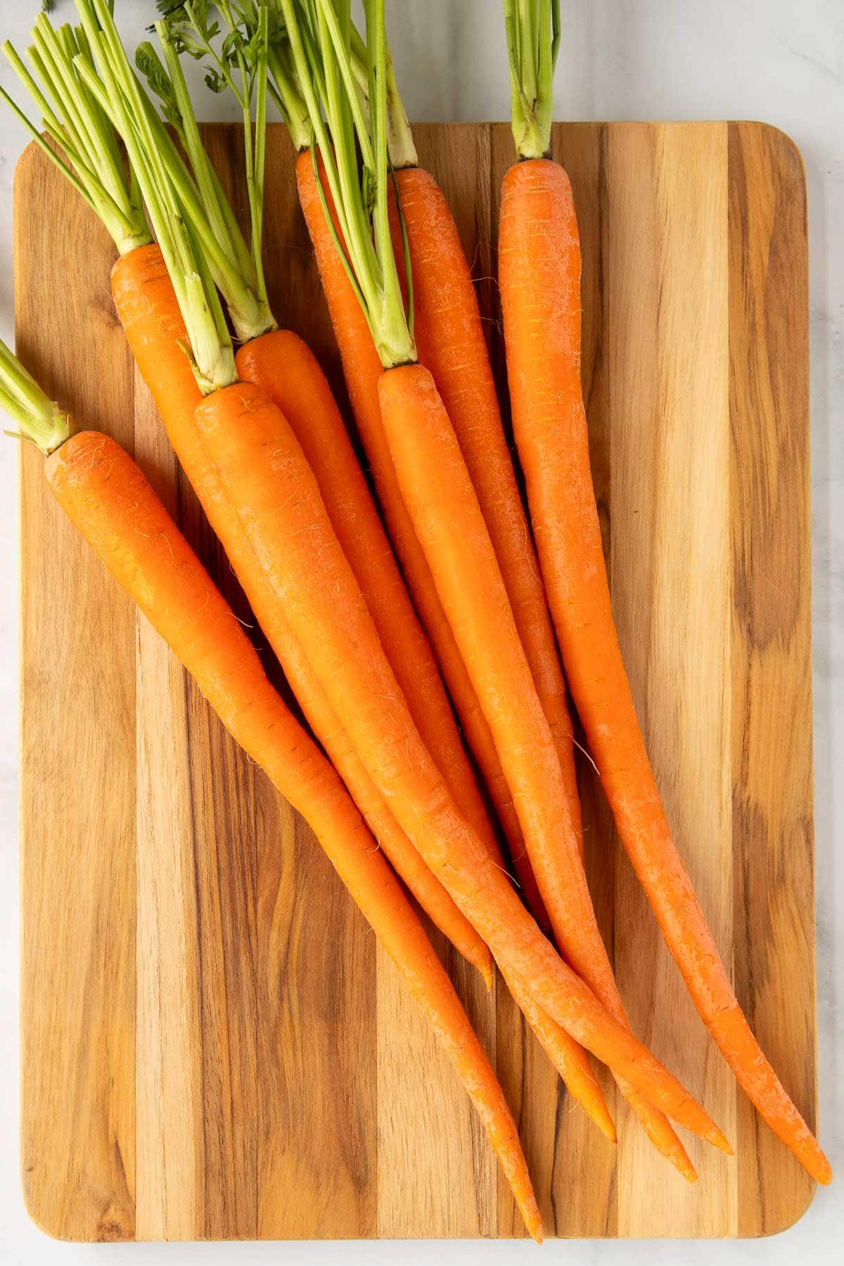 A bunch of carrots with green tops on a cutting board.