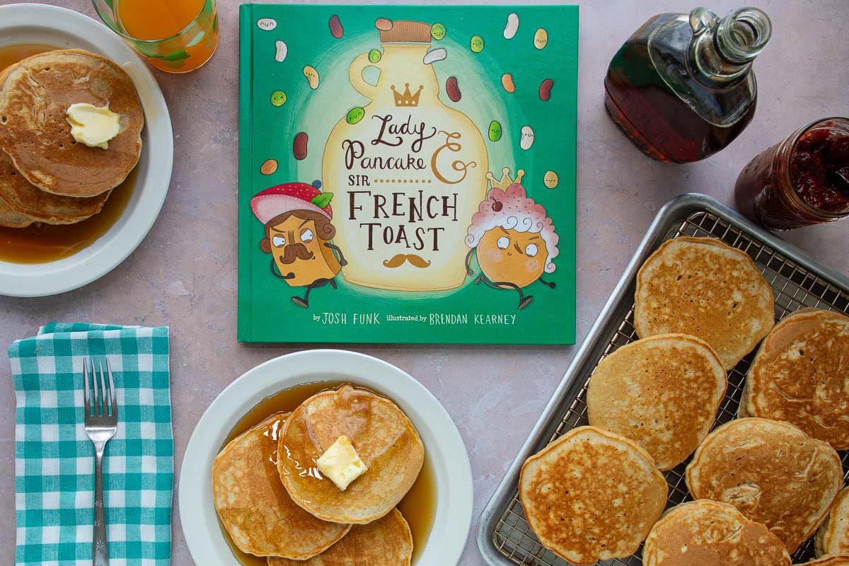 Two plates and a tray of pancakes with syrup next to the cover of the book Lady Pancake & Sir French Toast.