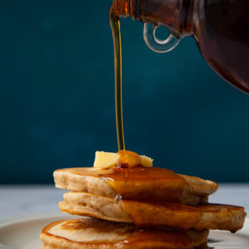 Maple syrup pouring over a stack of French toast pancakes.
