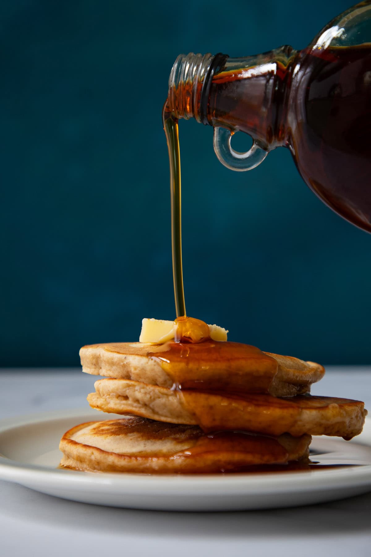 Maple syrup pouring over a stack of French toast pancakes.