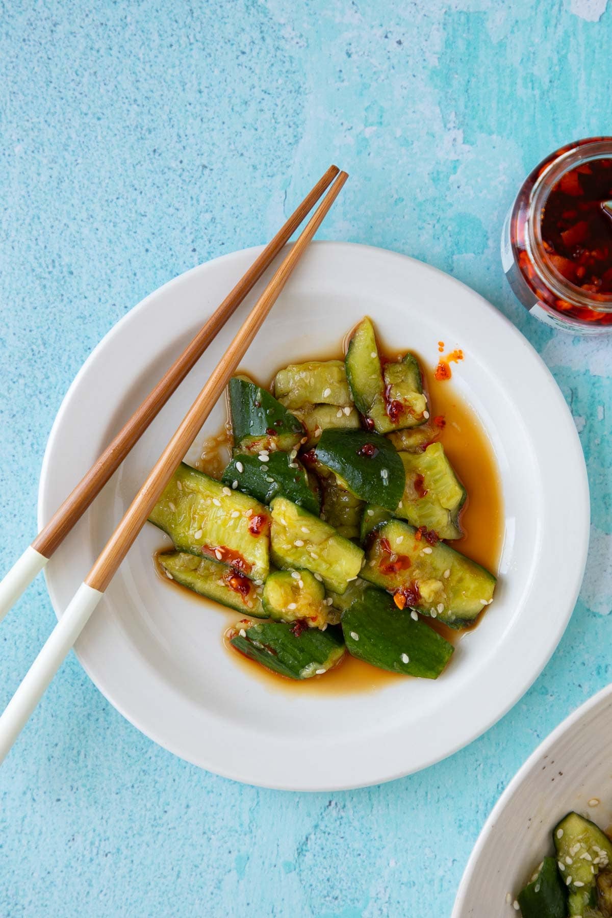 A serving of smashed cucumber salad with chopsticks and a jar of chili crisp nearby.