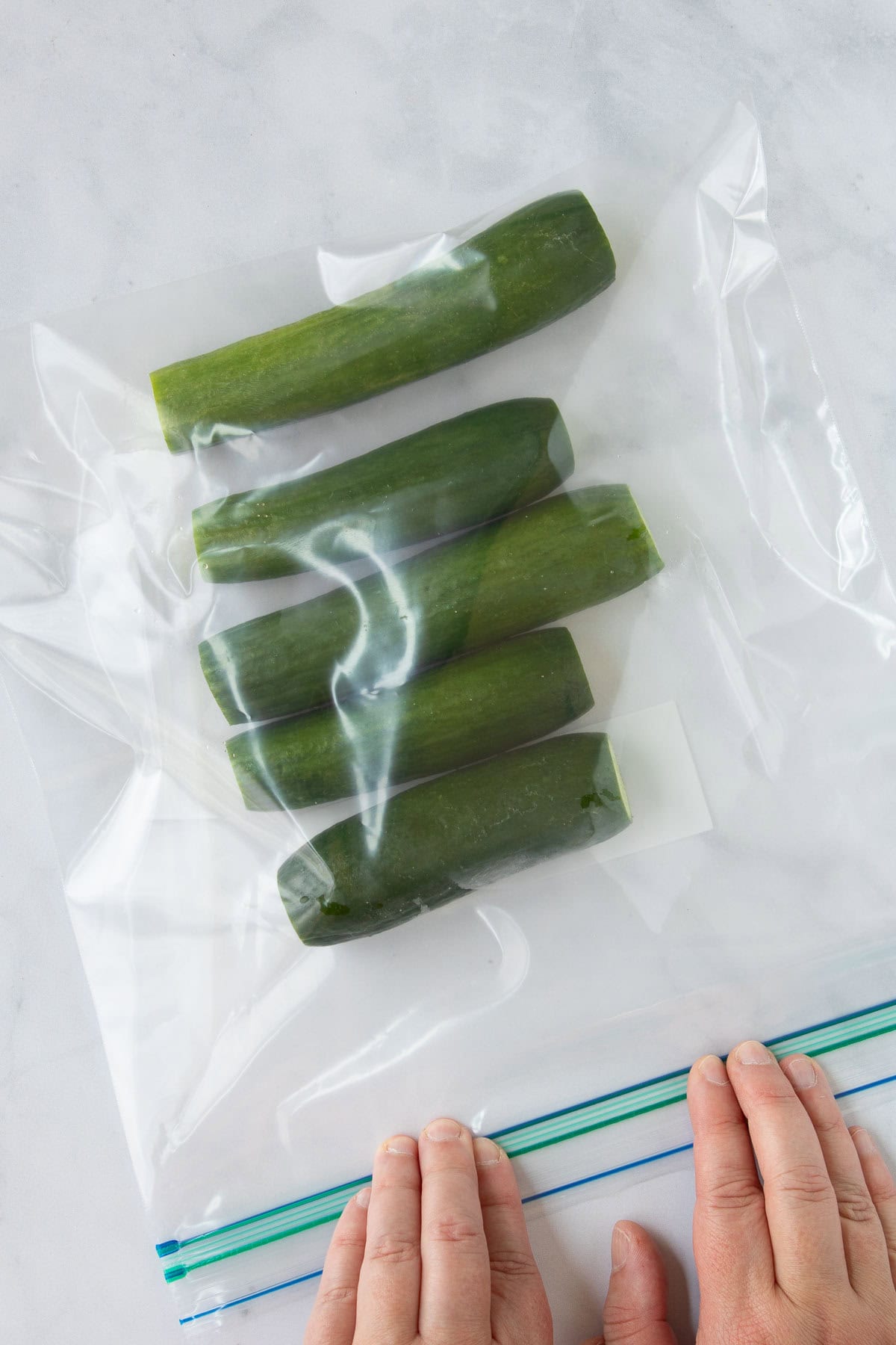 Hands closing a zip-top bag full of small cucumbers.