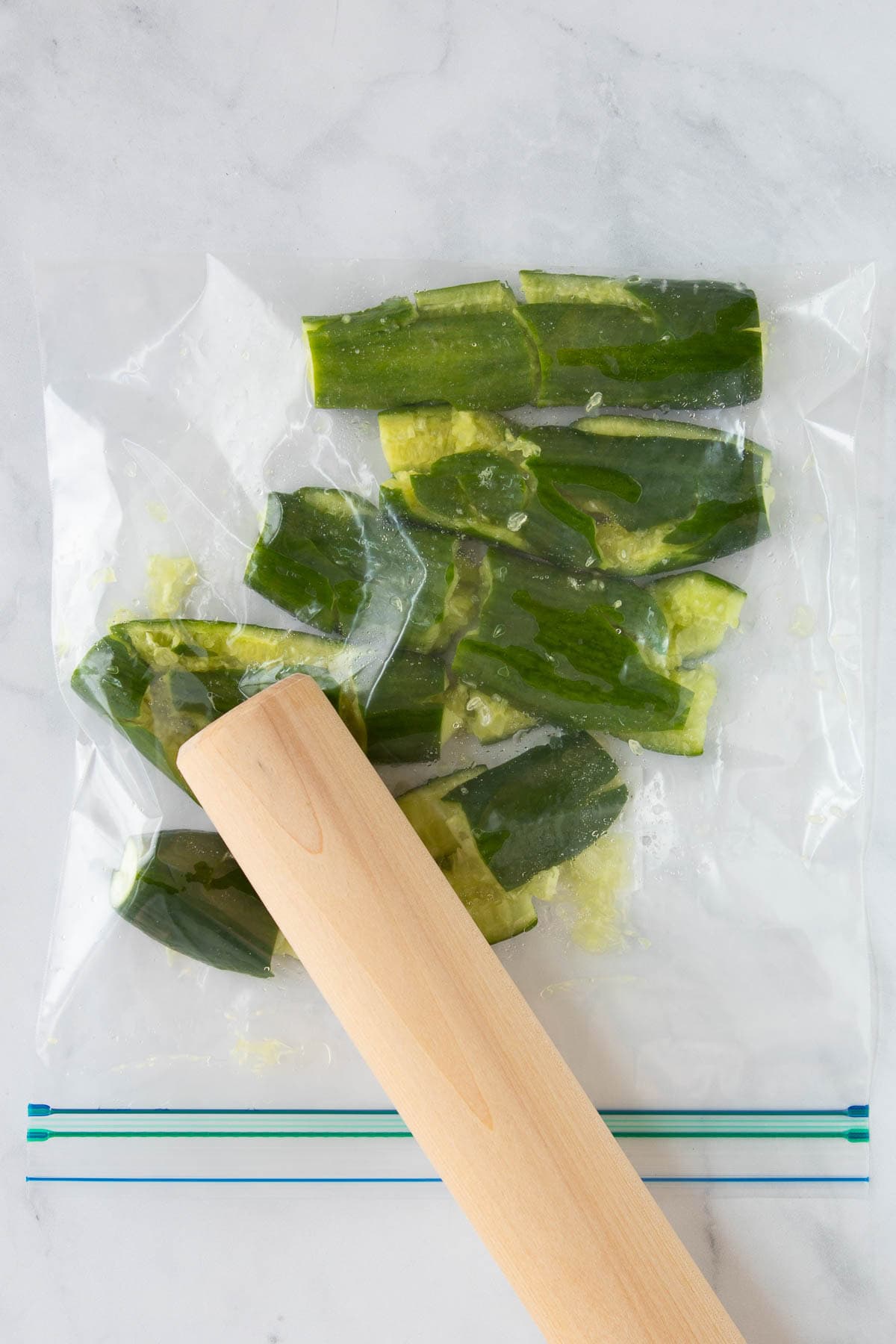 Cucumbers being smashed in a zip-top bag with a rolling pin.