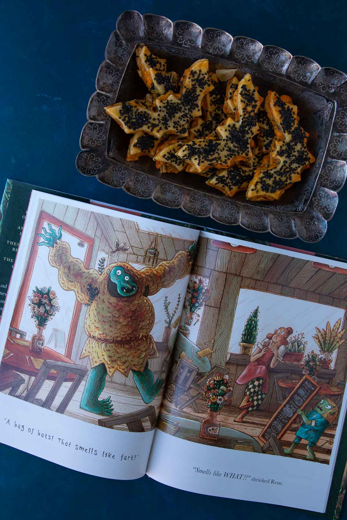 The book The Cafe at the Edge of the Woods open to a page, next to a tray of cheddar-artichoke bat tarts.