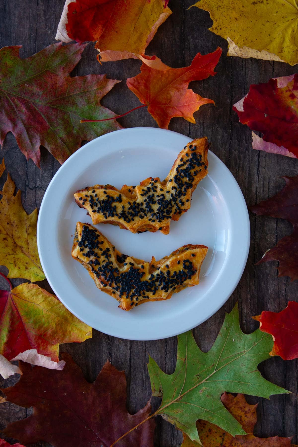 A plate of cheddar-artichoke bat tarts, surrounded by colorful fall leaves.