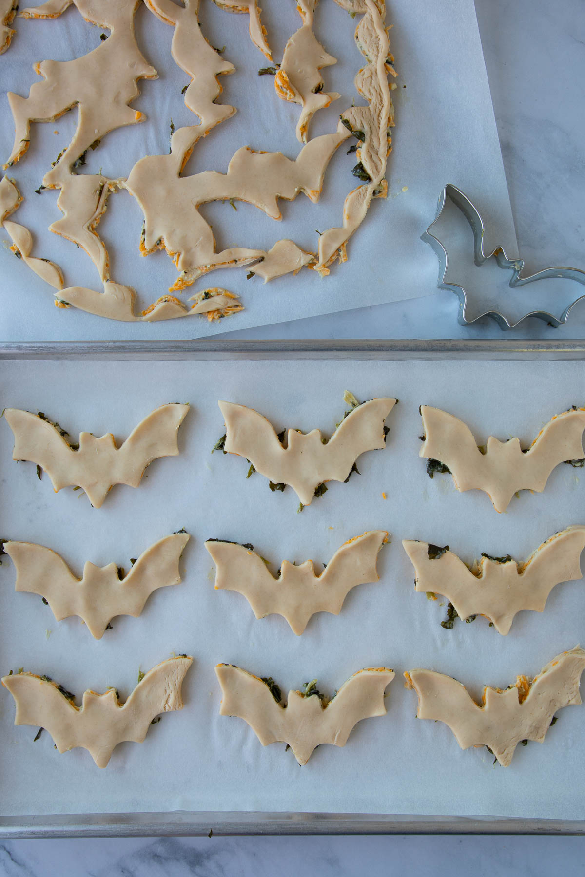 Unbaked cheddar-artichoke bat tarts on a parchment-lined baking sheet.