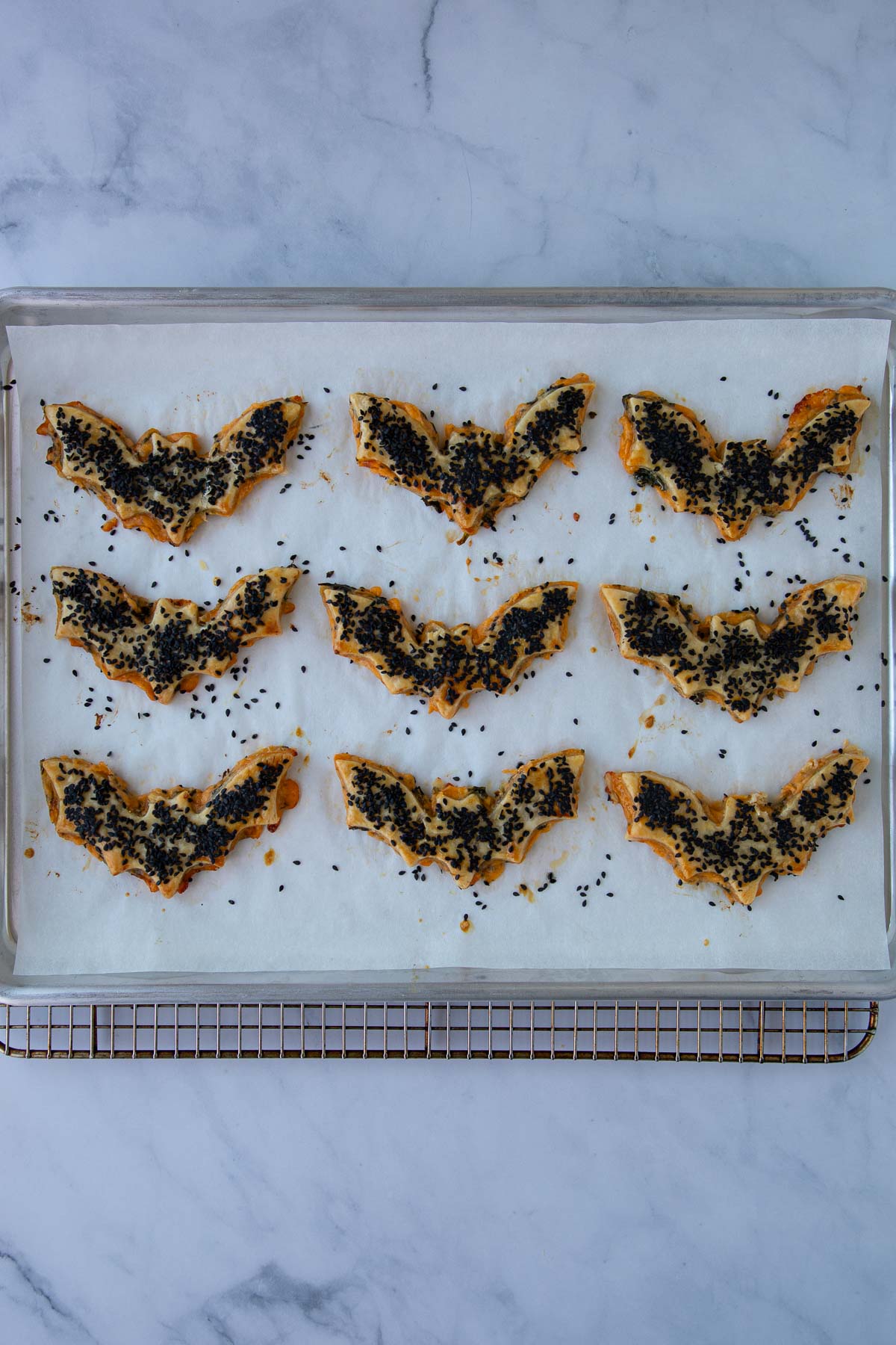 Baked cheddar-artichoke bat tarts on a parchment-lined baking sheet.